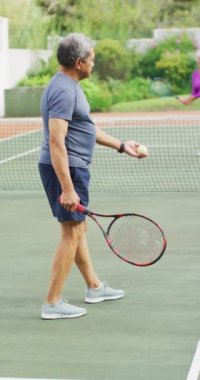 Tenis kortunda oynayan mutlu çift ırklı çiftin dikey videosu. sağlıklı, aktif emeklilik.