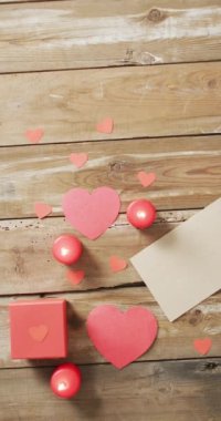 Yanan kırmızı mumlar, kırmızı kalpler, ahşap masa üstündeki hediye ve harflerin dikey görüntüsü. Sevgililer Günü, romantizm ve kutlama.