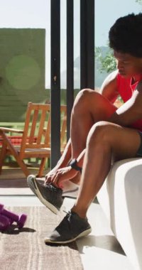 Spor yapmadan önce spor ayakkabısı giyen Afro-Amerikan bir adamın dikey videosu. sağlıklı aktif yaşam tarzı ve evdeki uygunluk, beden içeriği.