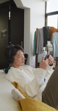 Oturma odasında video oyunu oynayan Asyalı bir gencin dikey videosu. Evde yalnız zaman geçirmek..