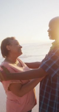 Sunny Beach 'te sarılan mutlu Afrikalı Amerikalı çiftin dikey videosu. Plaj tatilinde boş zaman geçirmek.