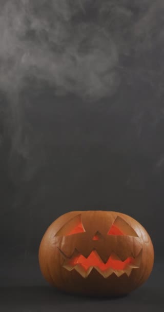 ライト付きの垂直ビデオは灰色の背景に煙の雲とハロウィンのカボチャを彫刻しました ハロウィン お祝いのコンセプト — ストック動画
