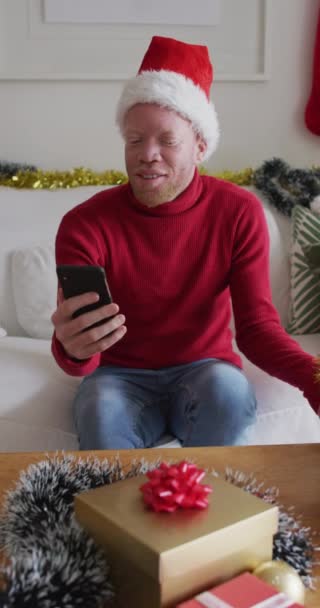 Вертикальный Снимок Альбиноса Видеозвонком Шляпе Санта Клауса Показывающего Завернутый Подарок — стоковое видео