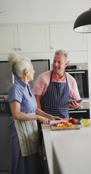 キッチンでのシニア白人夫婦の料理の垂直ショット 野菜をカットし タブレットを使用して 高齢者と家庭生活の概念 — ストック動画