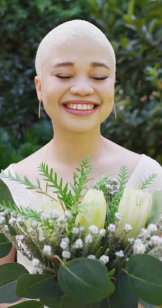 晴れた日に庭で花の束を持つ幸せな出産の女性の肖像画の垂直ビデオ 結婚式の日とお祝いのコンセプト — ストック動画