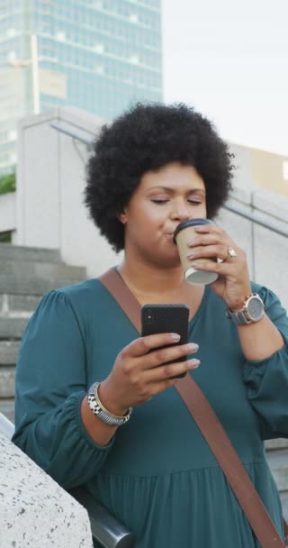 コーヒーとスマートフォンで通りを歩くプラスサイズの出産女性の垂直ビデオ 都市に住んでエラーを実行しています — ストック動画