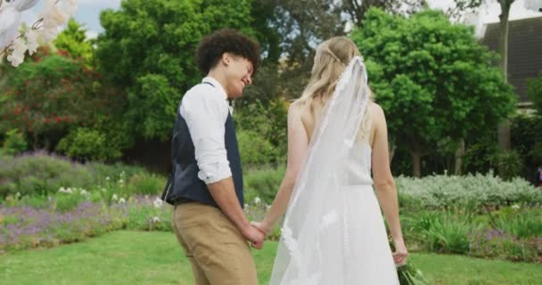 結婚式で晴れた日に庭を歩く幸せな多様なカップル 屋外結婚式 パーティー お祝いのコンセプト — ストック動画