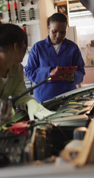 2つの多様な女性の車の力学チェック車の垂直ビデオ 車修理工場で働き女性らしい小さなビジネスコンセプトを運営しています — ストック動画