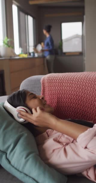 ソファの上で音楽を聴いてヘッドフォンで幸せな出産の女性の垂直ビデオ 家で一緒に質の高い時間を過ごす — ストック動画