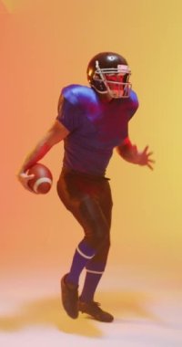 Kafkas erkek Amerikan futbolcusunun neon turuncu ışıklandırmalı topu tutuşu. Spor, hareket, eğitim ve aktif yaşam tarzı kavramı.