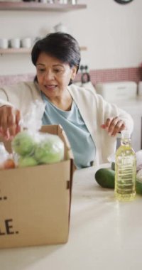 Sadece mutfaktaki kutudan sebze alan yaşlı melez kadının dikey videosu. evde sağlıklı ve aktif emeklilik.