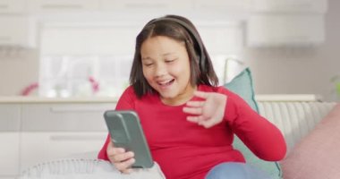 Kanepede akıllı telefonuyla dinlenen mutlu Asyalı kızın videosu. Çocukluk, rahatlama, evde teknoloji konseptiyle zaman geçirme.