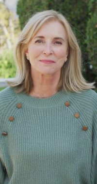 Bahçede kameraya gülümseyen sarı saçlı, mutlu, beyaz bir kadının dikey video portresi. Dijital olarak üretilen ev hayatı, sağlık ve mutluluk konsepti.