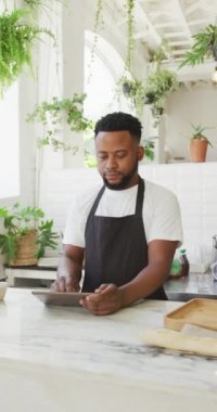 Kafede gülümseyen ve tablet kullanan Afro-Amerikan erkek kahveci portresinin dikey videosu. global işletme ve kahveci kafe.