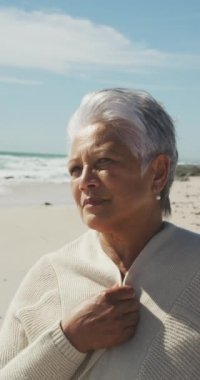 Güneşli sahilde tek başına mutlu bir melez kadının dikey videosu. sağlıklı, aktif emeklilik plaj tatili.