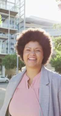 Caddedeki kameraya gülümseyen mutlu ve melez bir kadının dikey videosu. Şehirde yaşıyor ve ayak işlerini yapıyor..