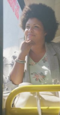 Minibüste pencereden dışarı bakan mutlu ve melez bir kadının dikey videosu. Şehirde yaşıyor ve ayak işlerini yapıyor..