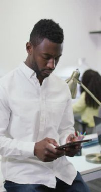 Afro-Amerikan bir adamın iş yerinde tablet kullandığı dikey bir video. Yaratıcı bir işte, iş yerinde bedensel bütünlük.