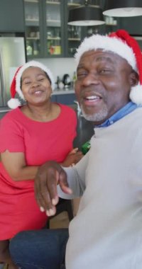 Yaşlı bir Afro-Amerikan çiftin, Noel Baba şapkası takıp kameraya öpücük gönderdikleri dikey bir fotoğraf. Son sınıflar ve Noel konsepti.
