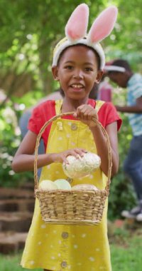 Vertical video of portrait of happy african american girl at easter in garden. family spending time together at home.