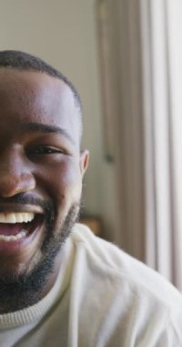 Vertical video of half the face of happy african american man laughing to camera. Domestic life, health, happiness and inclusivity concept.