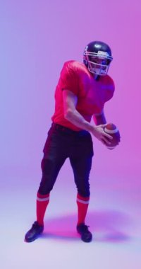 Kafkasyalı erkek Amerikan futbolcunun topu tuttuğu dikey video, neon ışıklı. Spor, hareket, eğitim ve aktif yaşam tarzı kavramı.