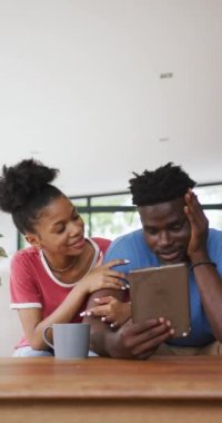 Evde tablet kullanan mutlu Afro-Amerikan çiftin dikey videosu. Evde birlikte vakit geçirmek..