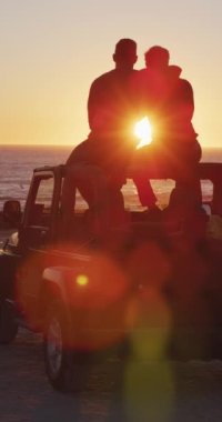 Siluetli eşcinsel bir çiftin arabada oturup gün batımını seyredip kucaklaşmalarını gösteren dikey bir video. Romantik yolculuk, seyahat ve özgürlük.