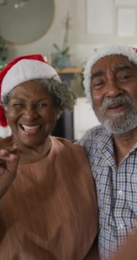 Yaşlı bir Afro-Amerikan çiftin Noel Baba şapkası takıp video görüşmesi yaparken dikey çekimleri. Yaşlılar, teknoloji ve Noel konsepti.