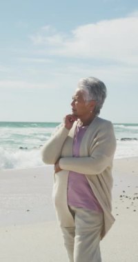 Güneşli sahilde tek başına mutlu bir melez kadının dikey videosu. sağlıklı, aktif emeklilik plaj tatili.