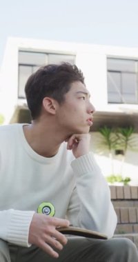 Asyalı bir gencin bahçede kaykayıyla oturduğu dikey bir video. Evde yalnız zaman geçirmek..