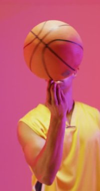 Çift ırklı erkek basketbolcunun pembe arka planda dönen topunun dikey videosu. Spor ve rekabet konsepti.