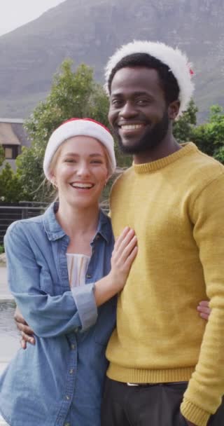 屋外でクリスマスを祝うサンタの帽子の多様な幸せなカップルの垂直ビデオポートレート クリスマス お祝い 包括性とライフスタイルの概念 — ストック動画