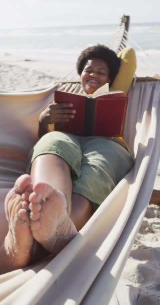 Vídeo Vertical Mulher Afro Americana Lendo Livro Sobre Rede Praia — Vídeo de Stock