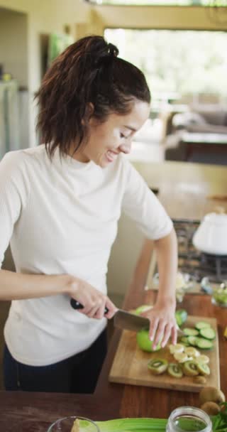 在厨房里放着一个垂直的视频 照片上是一个笑着的白桦树女人 手里拿着白杨树切果 身体包容 健康的生活方式 在家里享受闲暇时间 — 图库视频影像