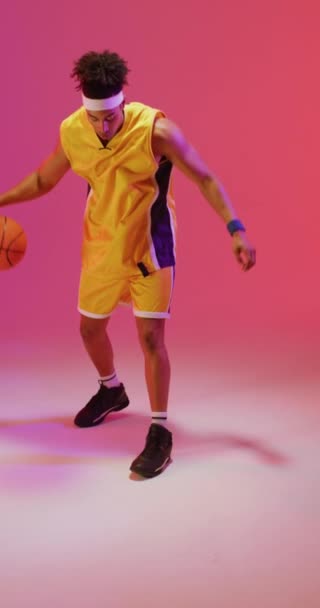 ピンクの背景にボールを跳ねる出生男性バスケットボール選手の垂直ビデオ スポーツ 競技の概念 — ストック動画
