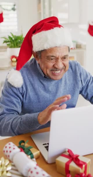 サンタの帽子の幸せなシニアの出産男の垂直ビデオは ラップトップ上でクリスマスのビデオ通話を行います クリスマス グローバルなコミュニケーション 包括性とシニアライフスタイルの概念 — ストック動画