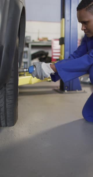 アフリカ系アメリカ人女性の自動車整備士の垂直ビデオタイヤを交換します 車修理工場で働き女性らしい小さなビジネスコンセプトを運営しています — ストック動画