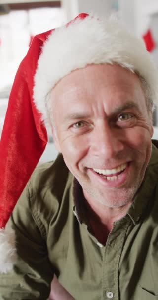 幸せな白人男性の垂直ビデオサンタの帽子をかぶって ビデオ通話をしています クリスマスに一人で家で過ごす — ストック動画
