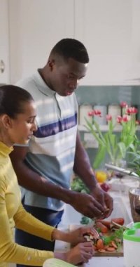 Mutfakta konuşan ve sebze kesen mutlu çiftin dikey videosu. Mutluluk, sağlık, ev hayatı ve kapsayıcılık kavramı.