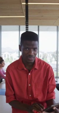 Modern ofiste arka planda meslektaşları olan gülümseyen Afrikalı Amerikalıların dikey videosu. Yaratıcı bir iş yerindeki bedensel kapsayıcılık.