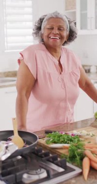 Mutfakta yemek pişiren mutlu Afrikalı Amerikalı kadının dikey videosu. Emeklilik ve ev kavramında zaman geçirme.