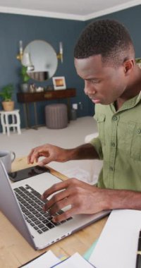 Yatak odasında bilgisayar ve akıllı telefon kullanarak çalışan Afrikalı bir Amerikalının dikey videosu. İletişim, evden çalışma, ev hayatı ve kapsayıcılık kavramı.