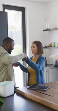 Vertical video of happy diverse couple having fun dancing together in kitchen. Domestic life, togetherness, health, happiness and inclusivity concept.