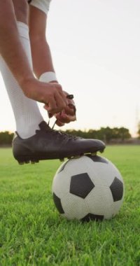 Sahada bağcıkları bağlayan çift ırklı futbolcunun dikey videosu. Erkek futbol takımı, kapsayıcılık ve takım sporlarına uygunluk.