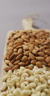 Badem ve kaju fıstıklarının dikey videosu ahşap doğrama tahtasına yığılmış ve eflatun arkaplanlı. sağlıklı beslenme, yemek ve beslenme.