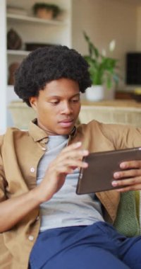 Afro-Amerikan bir adamın tablet kullanıp güldüğü dikey bir video. ev hayatı, beden katılımı, teknolojiyle evde kaliteli zaman geçirmek..
