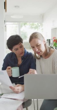 Evde dizüstü bilgisayarda çalışan beyaz lezbiyen çiftin dikey videosu. Evde birlikte vakit geçirmek..