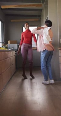 İki farklı genç kız arkadaşın dans edip evde eğlendiğini gösteren dikey video. Ev kavramında arkadaşlık ve kaliteli zaman geçirme.