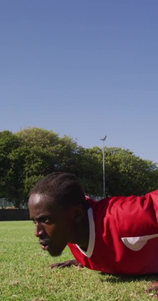 フィールド上のアフリカ系アメリカ人サッカー選手の垂直ビデオがプッシュアップを行う 男性サッカーチーム チームスポーツの包括性とフィットネス — ストック動画